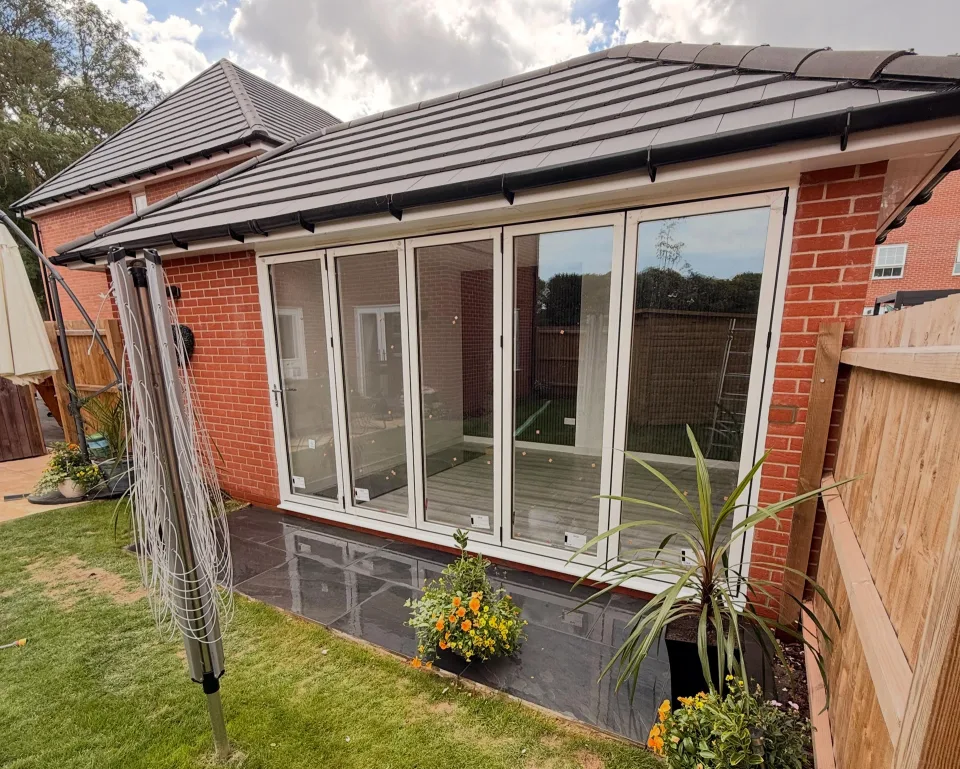A finished garage conversion with folding glass doors, a tiled roof and a new patio